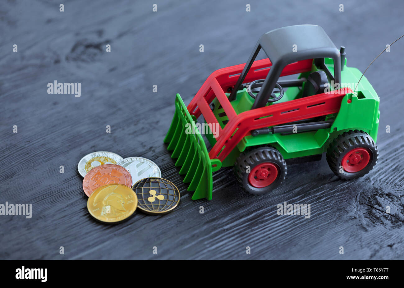 Un jouet tracteur pièces râteaux de crypto monnaie sur un fond en bois  noir, bitcoin : lightcoin, ondulation. Le concept du jeu avec crypto- monnaies Photo Stock - Alamy