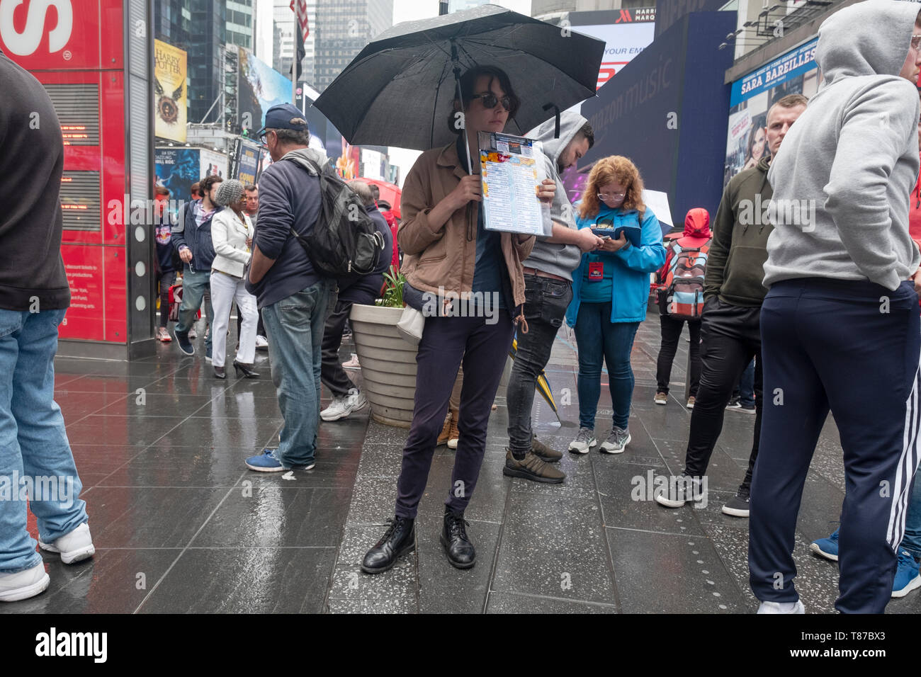 Sur un samedi pluvieux, une jolie jeune femme remise pour la vente des billets de théâtre, principalement pour les touristes. Times Square, Manhattan, New York. Banque D'Images