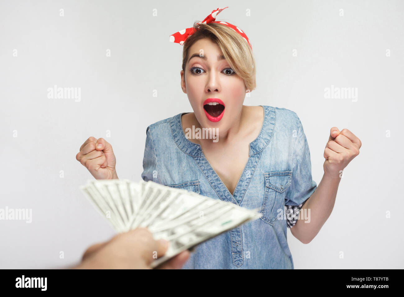 Aucun moyen. Surpris belle jeune femme en chemise en jean décontracté et bandeau rouge debout avec les bras levés et incroyable de grands yeux, gagné beaucoup d'argent. Banque D'Images