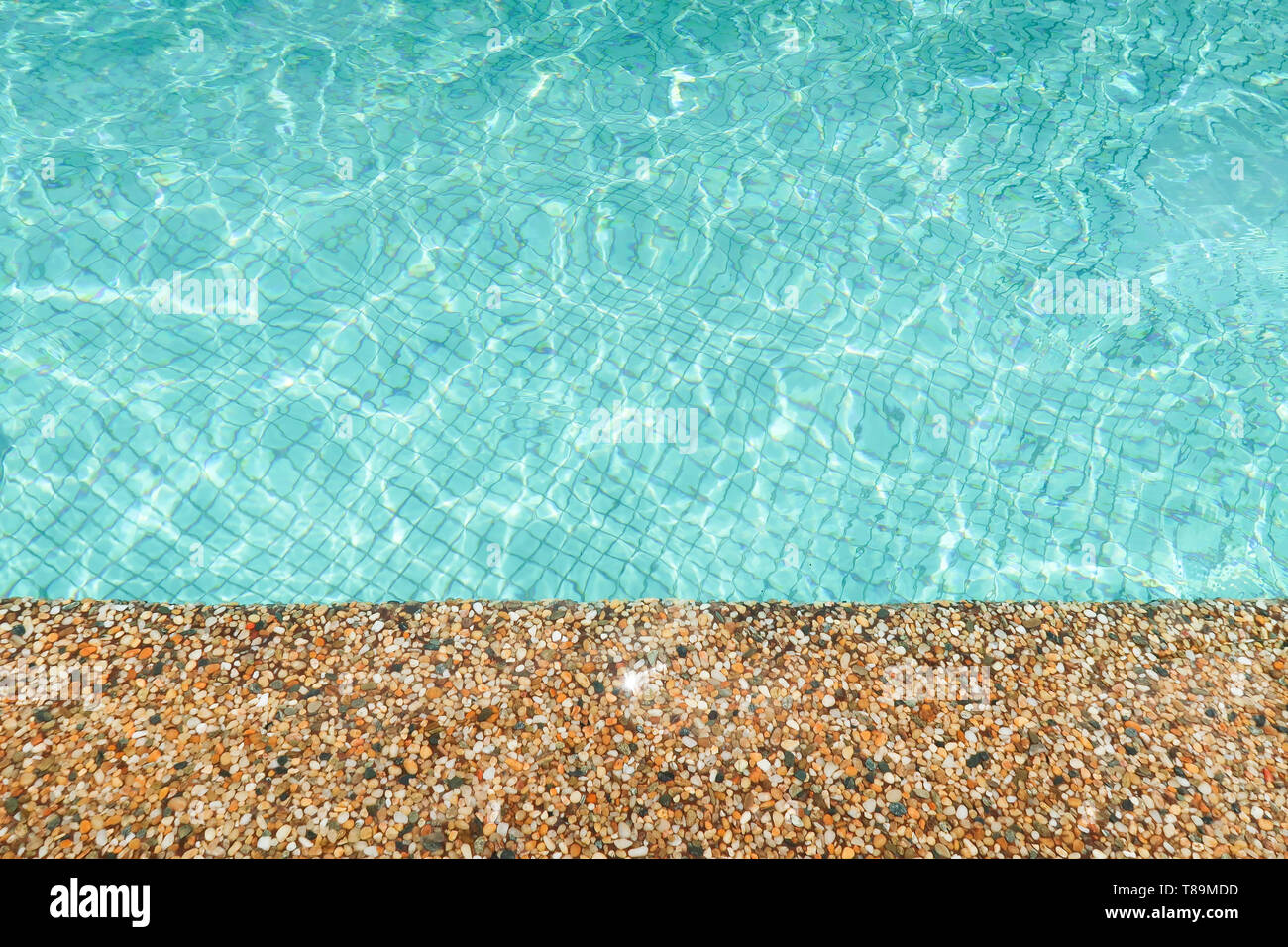 Rebord en pierre d'une piscine avec de l'eau brillant turquoise avec la réflexion du soleil Banque D'Images