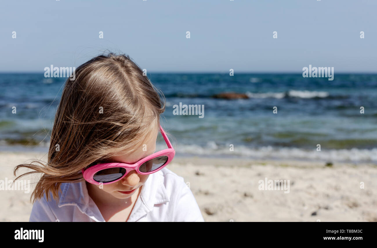 Funny little girl (7 ans) en lunettes se trouve sur la plage. Focus sélectif. Banque D'Images