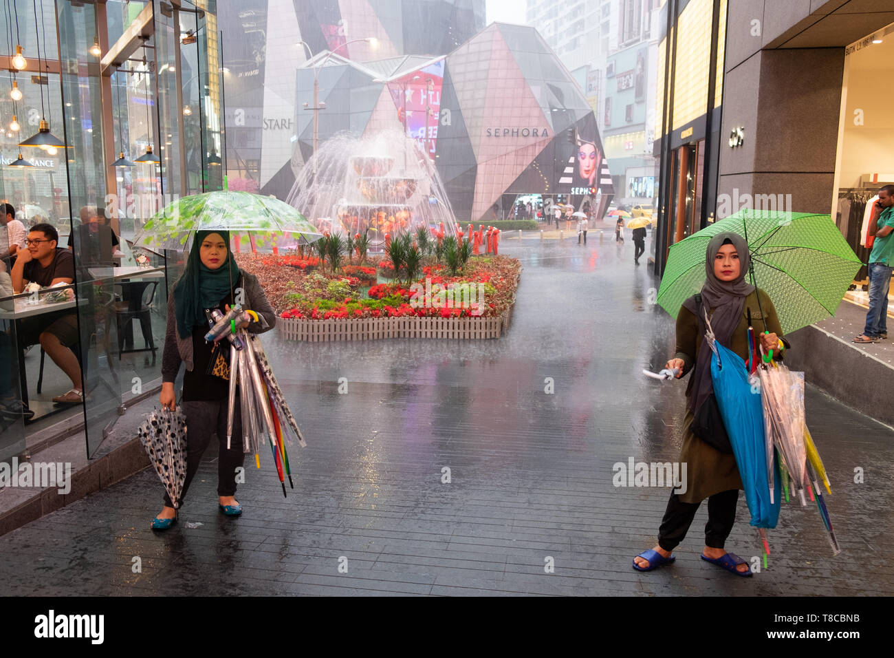 Deux femmes vendant des parapluies pendant une douche à effet pluie à l'entrée du centre commercial à Kuala Lumpur, Malaisie Banque D'Images