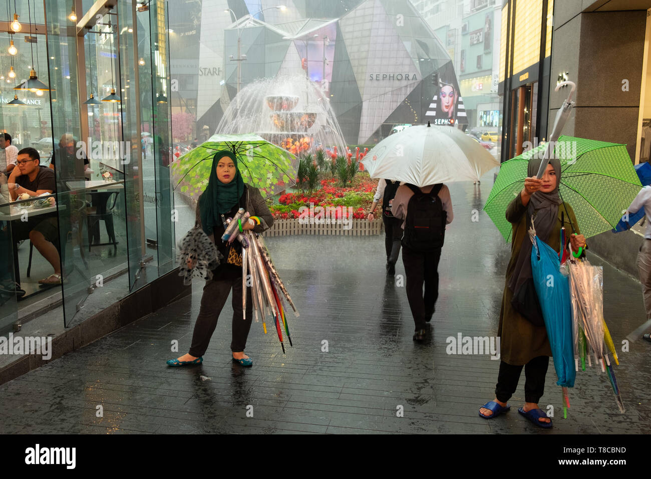 Deux femmes vendant des parapluies pendant une douche à effet pluie à l'entrée du centre commercial à Kuala Lumpur, Malaisie Banque D'Images