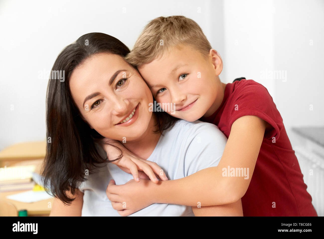Portrait of happy, joyeux écolier et sa mère posant en classe. Bel enfant debout, serrant maman, smiling, looking at camera. Notion de famille. Banque D'Images