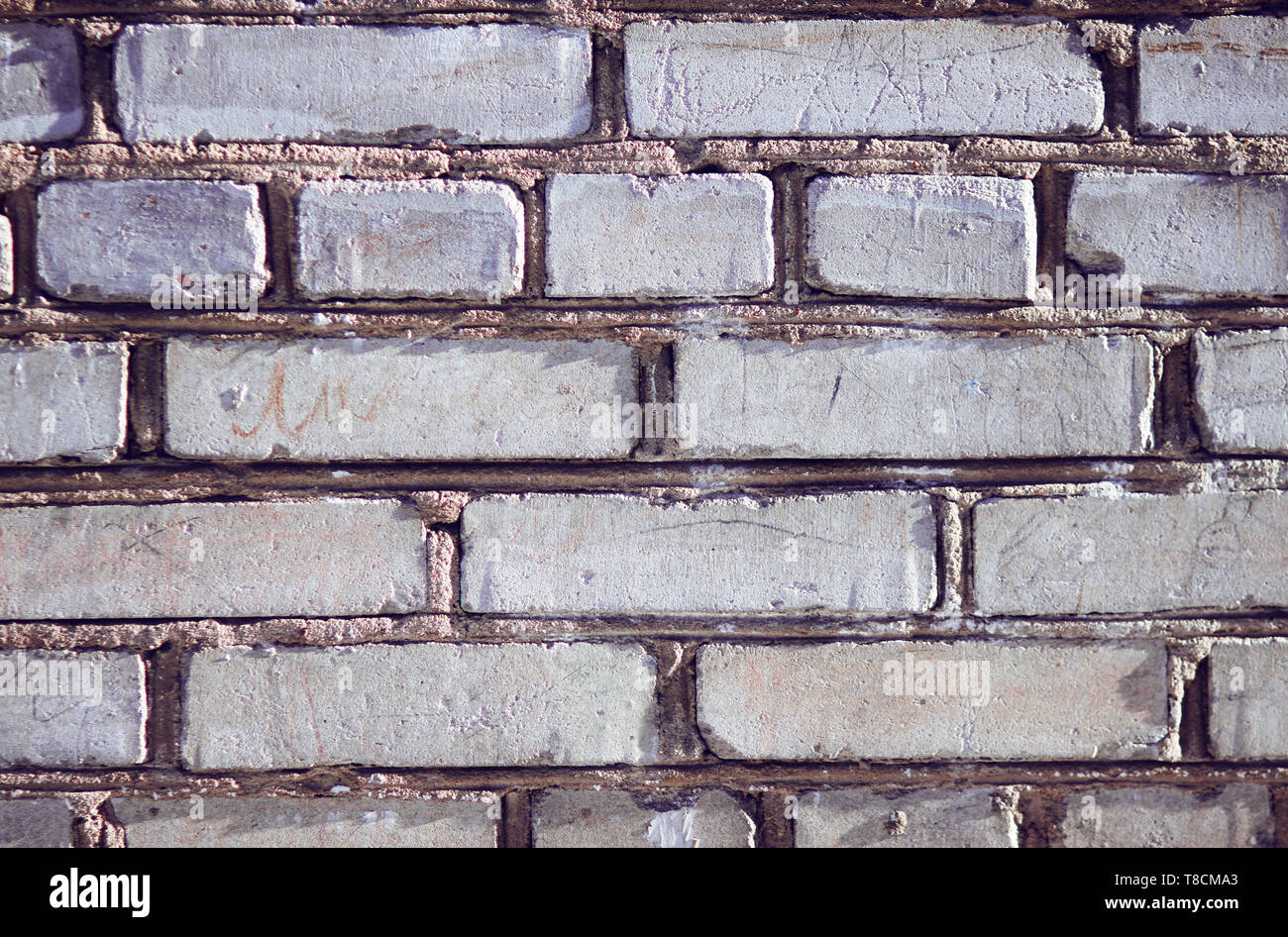 Le mur gris de l'immeuble, construit de briques inégales, est éclairée par le soleil et les colorer avec des crayons et inscriptions Banque D'Images