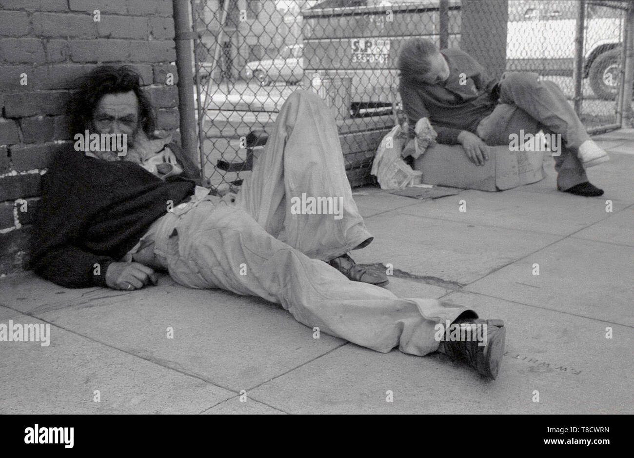 Années 1970, USA, Los Angeles, gens de la rue, deux hommes sans-abri allongé sur le trottoir, l'un assis sur une boîte en carton. Certaines parties de la région connue sous le nom de 'ville' en carton sont témoin d'un grand nombre de sans-abri vivant une existence au jour le jour dans la rue. Banque D'Images