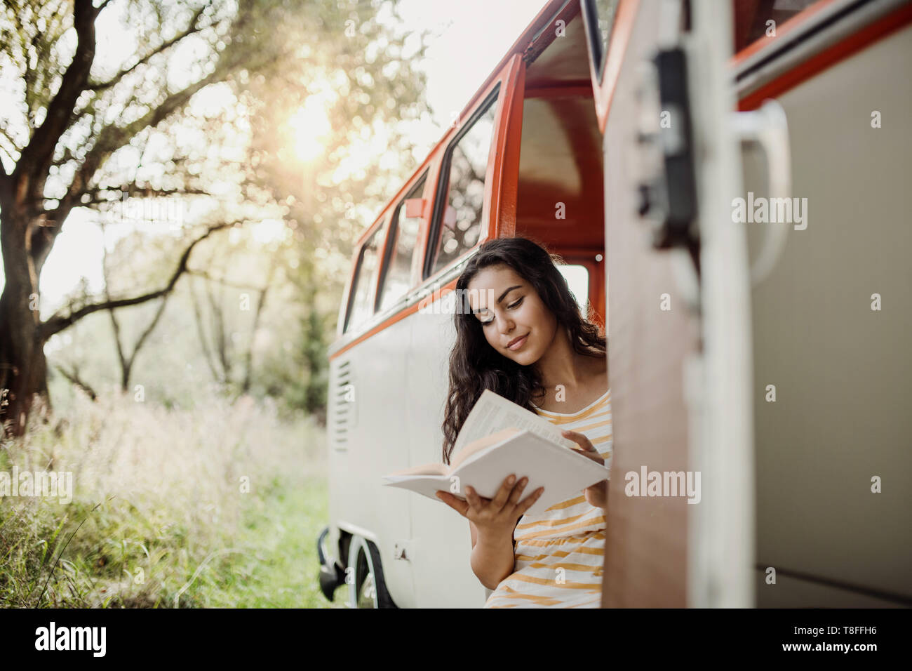 Une jeune fille avec un livre par une voiture sur un roadtrip à travers campagne, lecture. Banque D'Images