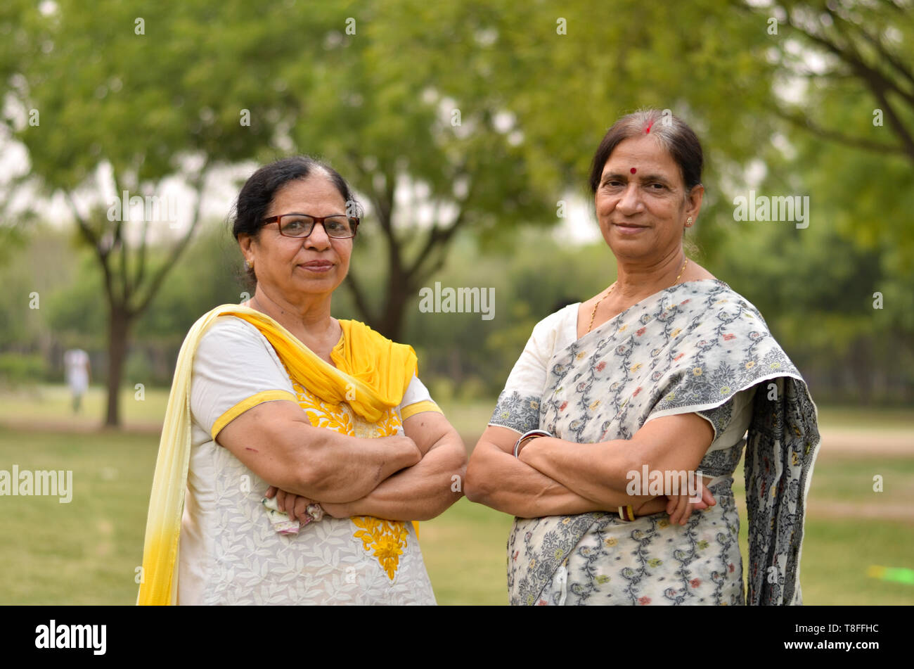 Portrait de deux femmes indiennes âgées amis femmes sœurs femmes debout dans un parc portant une saurée et salwar kameez avec des mains croisées / repliées pendant l'été Banque D'Images