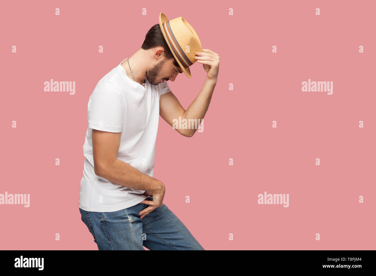 Vue côté profil portrait de jeune danseur barbu en chemise blanche homme tenant son chapeau et debout dans michael jackson danse posent. Piscine studio shot Banque D'Images