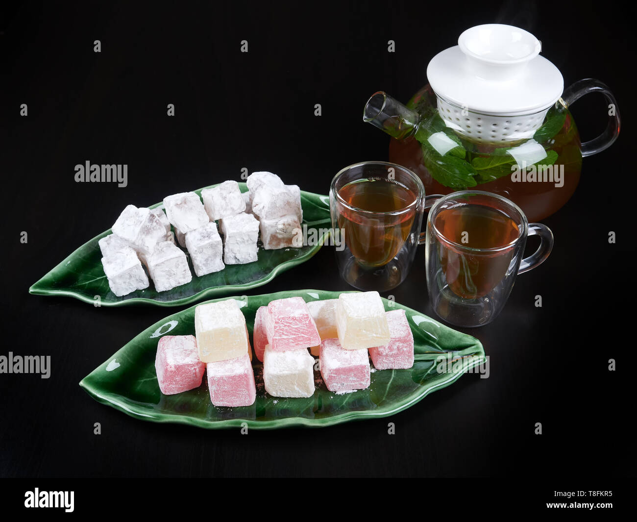 Loukoum sur un plateau en forme de feuille verte, servi avec du thé à la menthe, sur fond marron foncé Banque D'Images