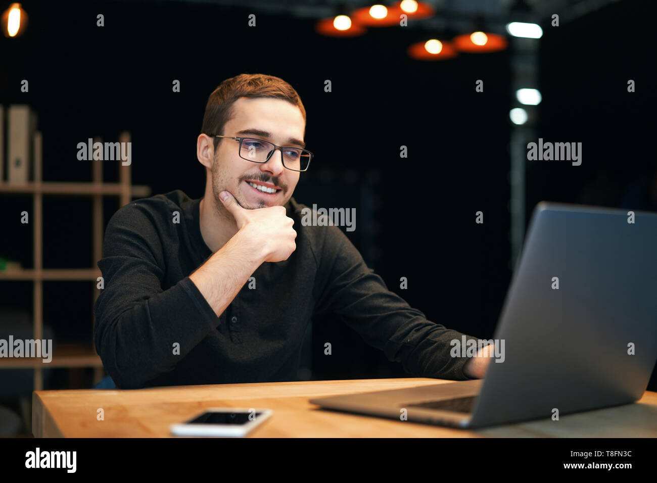 Jeune homme travailler avec ordinateur, téléphone et comprimé à la table tout en buvant du café Banque D'Images