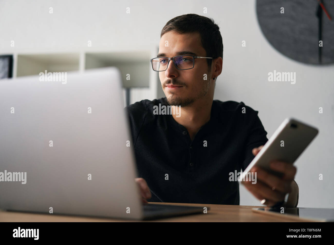 Jeune homme travaillant avec téléphone et ordinateur, réception d'appel téléphonique, parler avec les partenaires Banque D'Images
