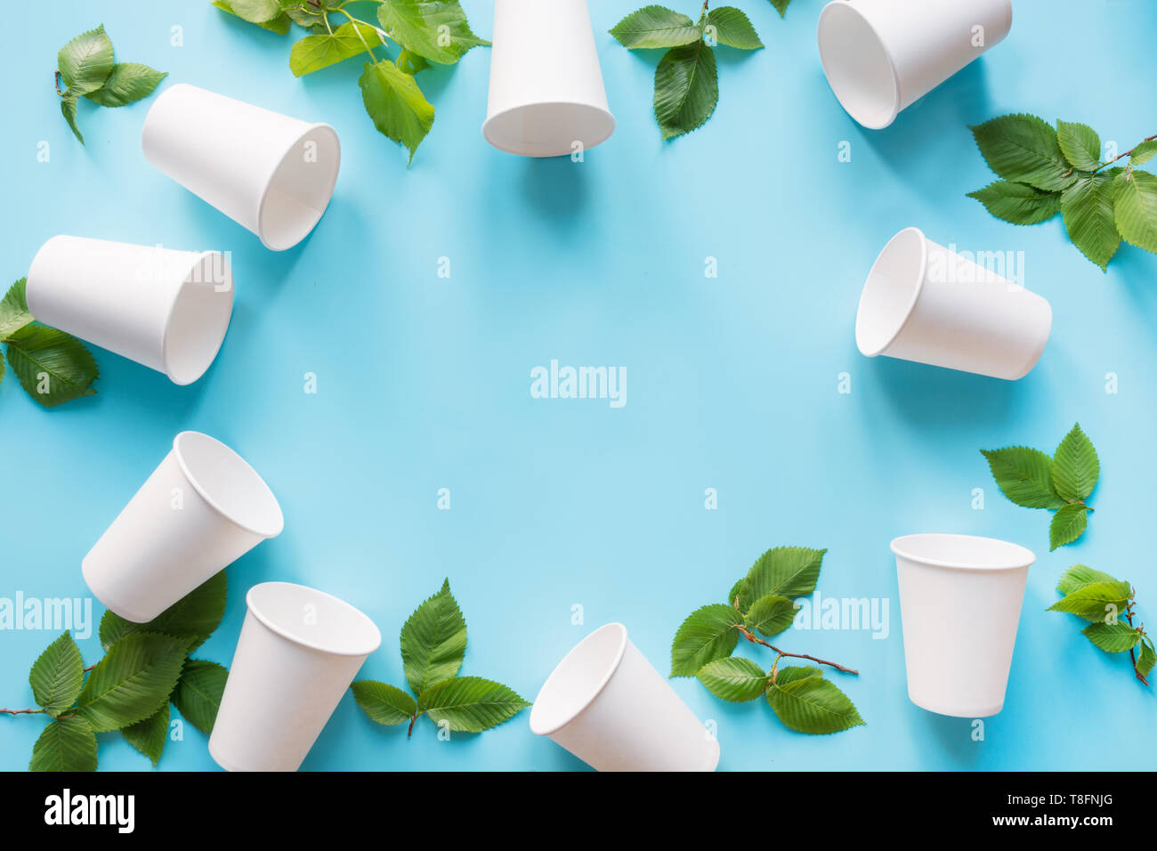 Frontière du gobelet jetable blanc et feuilles vertes sur fond bleu. Sauver la planète. Zéro déchets. Vue d'en haut Banque D'Images