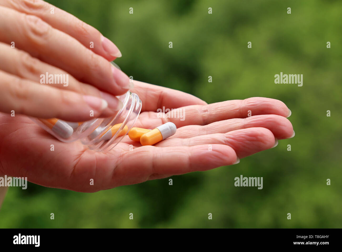 Femme avec des comprimés, les mains avec une bouteille de comprimés dans des capsules sur fond vert nature floue. Concept de vitamines pour la beauté, pour maigrir Banque D'Images
