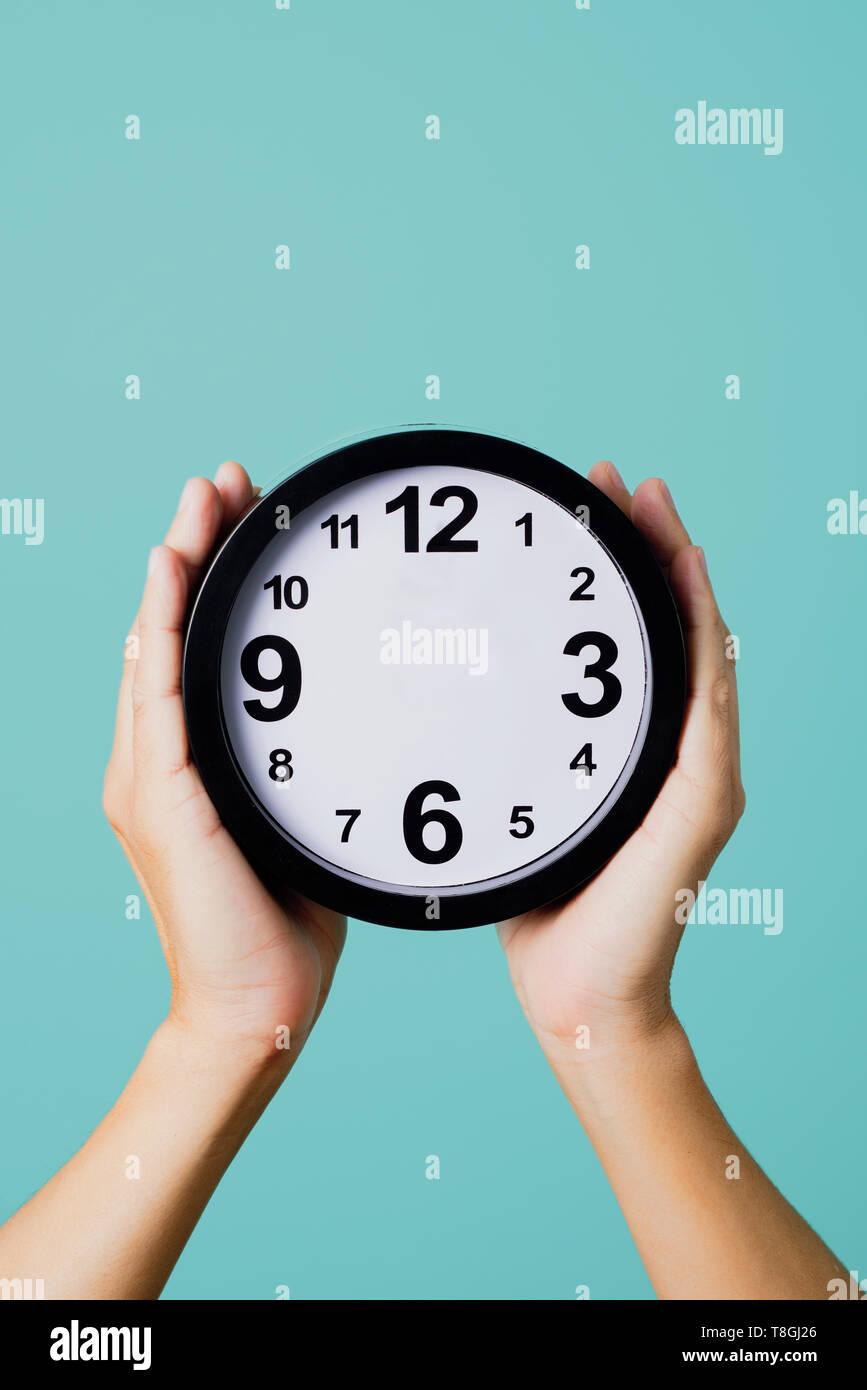 Les mains d'un young caucasian man holding une horloge, sans heure ou des minutes, sur un fond bleu, illustrant des concepts tels que de ne pas avoir de ti Banque D'Images