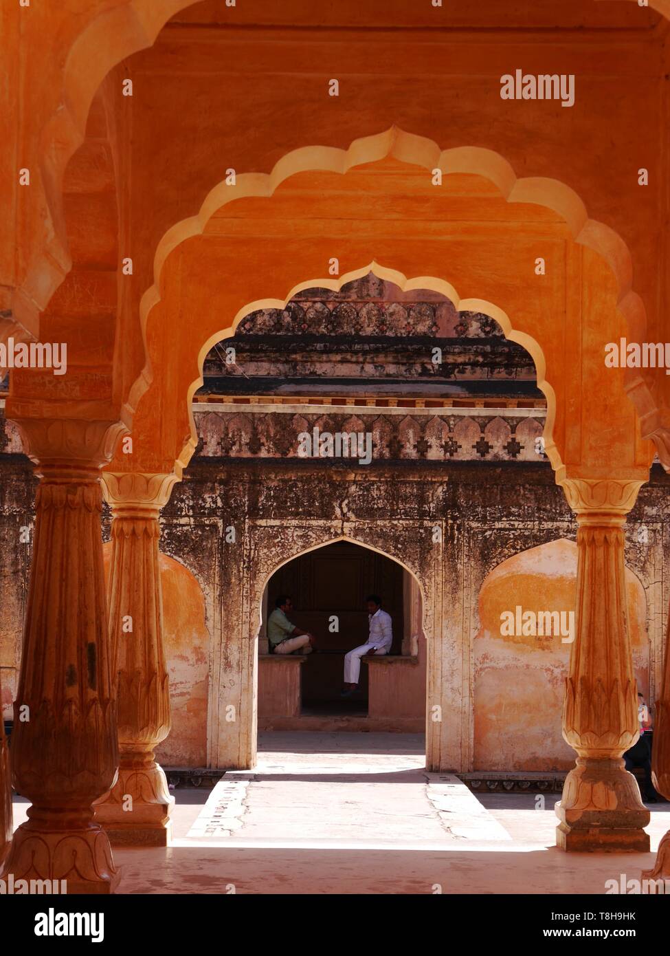 Vue à travers les arches de couleur ambre de deux jeunes hommes assis parlant dans un coin frais du Palais Ambre à Jaipur 'la ville rose', Rajasthan, Inde Banque D'Images