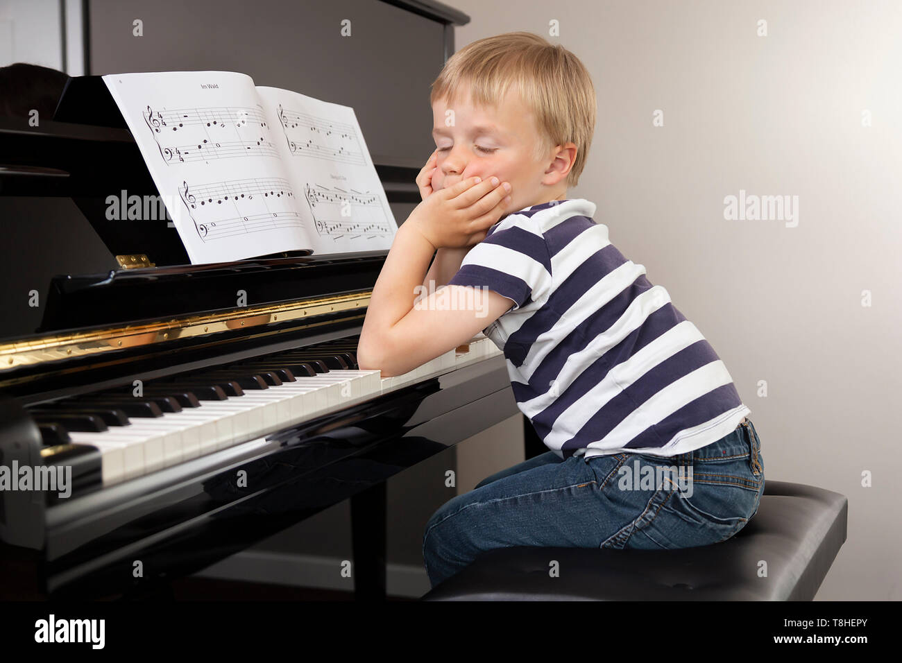Garçon, 4 ans, assis fatigué devant le piano Banque D'Images