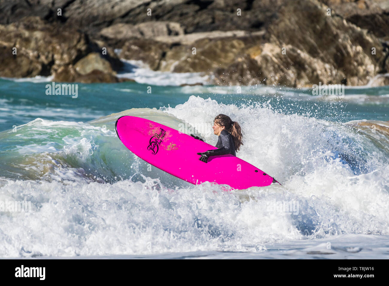 Une femme luttant pour le transport d'un surfeur en surf de grosses vagues à Newquay dans Fistral à Cornwall. Banque D'Images