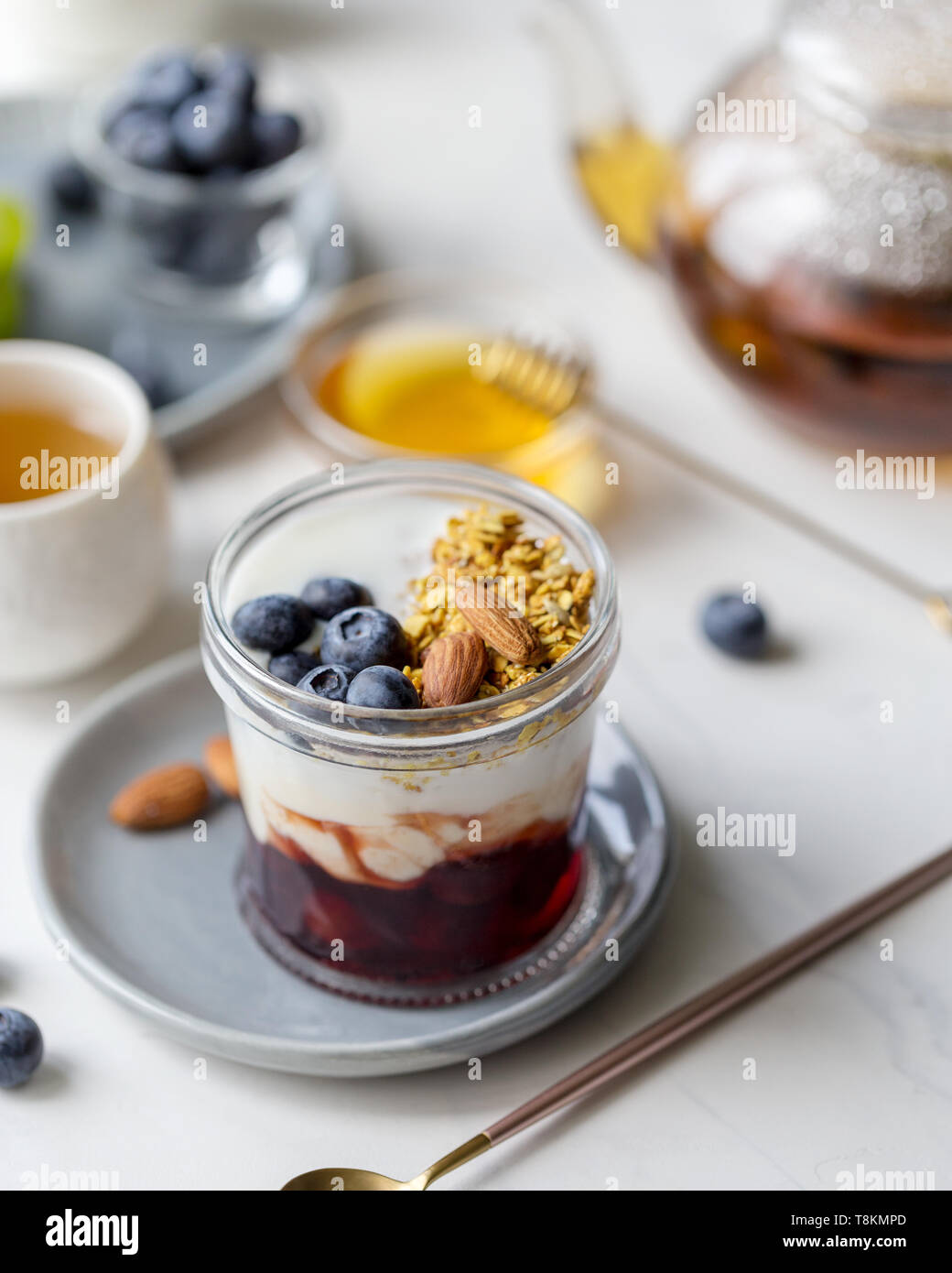 Petit-déjeuner sain frais granola avec avec de la confiture et des yaourts en pot avec des bleuets, avec du thé et du miel près de sur fond blanc Banque D'Images Petit-déjeuner sain frais granola avec avec de la confiture et des yaourts en pot avec des bleuets, avec du thé et du miel près de sur fond blanc Banque D'Images