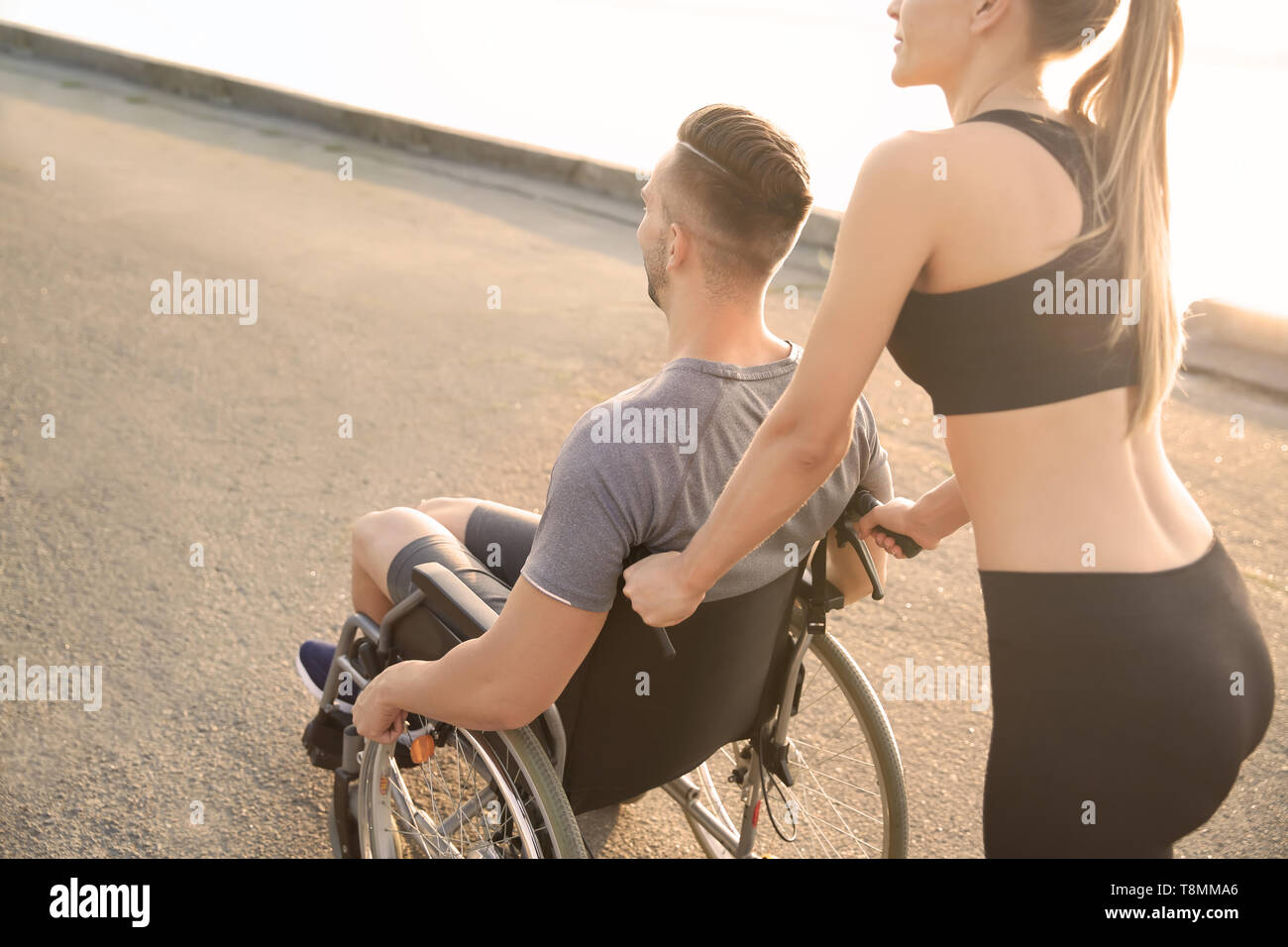 Femme sportive aider jeune homme en fauteuil roulant à l'extérieur Banque D'Images