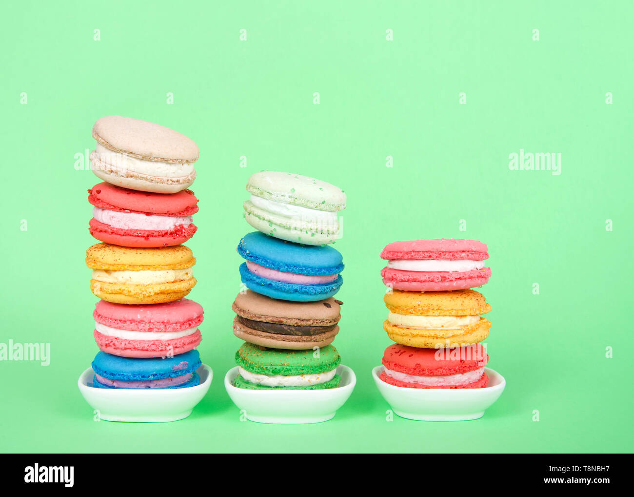 Macaron cookies dans de petits plats blanc empilés dans des lignes graduées, la pâtisserie française traditionnels colorés sur un fond vert menthe. Banque D'Images
