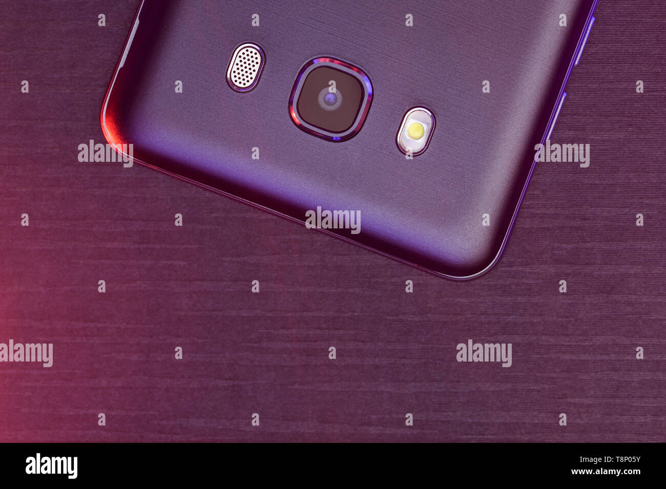 Un fragment de la téléphone cellulaire cas en noir avec rétroéclairage rose et pourpre. Le téléphone est sur noir tech surface nervurée rose appareil photo jusqu'éclairage. Banque D'Images