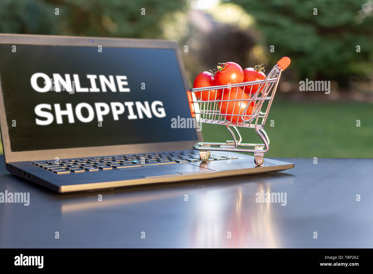 Concept de l'épicerie en ligne. Un petit panier avec des tomates est un permanent un ordinateur portable. Banque D'Images