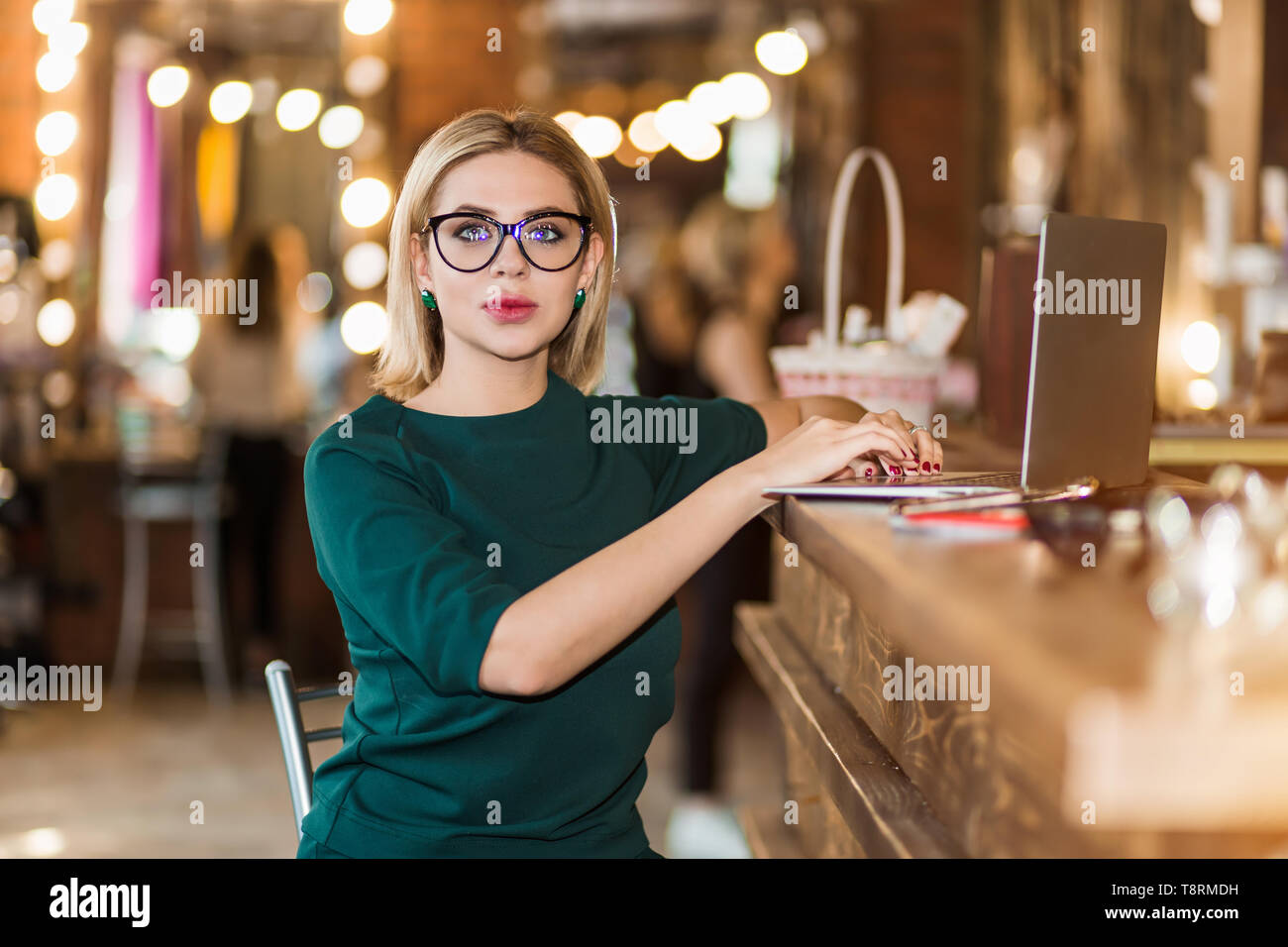 Portrait de salon de réceptionniste au travail. Charmante femme d'affaires graves en pull vert assis sur une chaise avec les mains sur le clavier, frappe, Banque D'Images