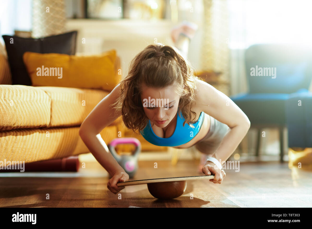 Fit woman in fitness vêtements dans le salon moderne faisant pompes à l'aide de balance board. Banque D'Images