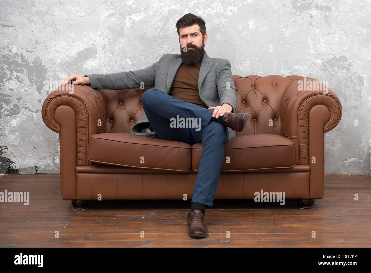 Louer appartement. Homme barbu avec confiance s'asseoir face à un canapé en cuir. Loft appartement intérieur. Le travail de l'agent immobilier d'affaires. Boutique de meubles. Agent immobilier Hipster style loft. Agent immobilier et location de vélos. Banque D'Images