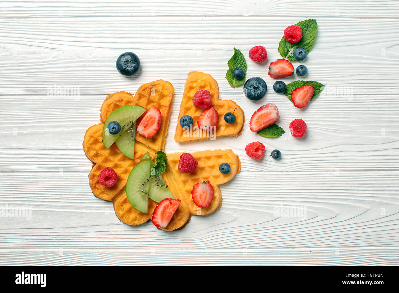 Gaufres en forme de coeur fruits rouges et tranches de kiwi sur fond de bois blanc Banque D'Images