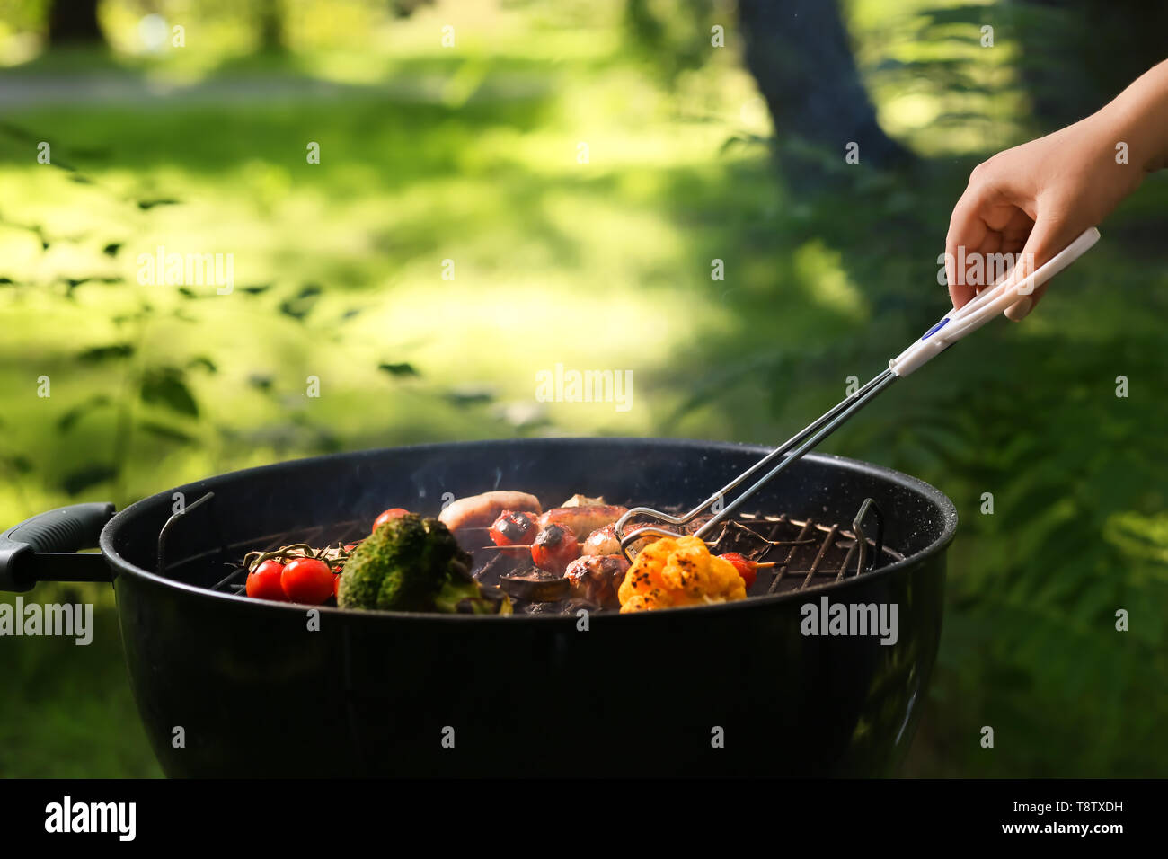 Woman cooking sausages et les légumes sur la grille du barbecue en plein air Banque D'Images
