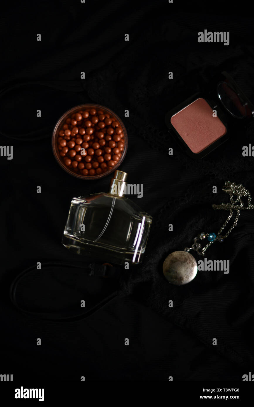 Collier pendentif, blush et bronzeur, un flacon de parfum sur un fond noir Banque D'Images