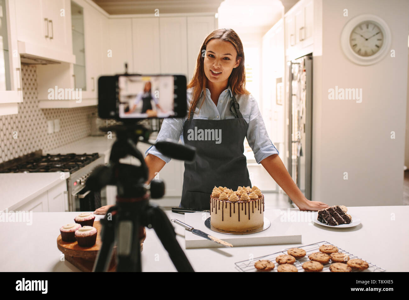 Jeune femme et l'enregistrement vidéo de cuisson vlogger pour food channel. Chef pâtissier femelle vlogging avec son téléphone mobile montée sur un trépied dans la cuisine. Banque D'Images