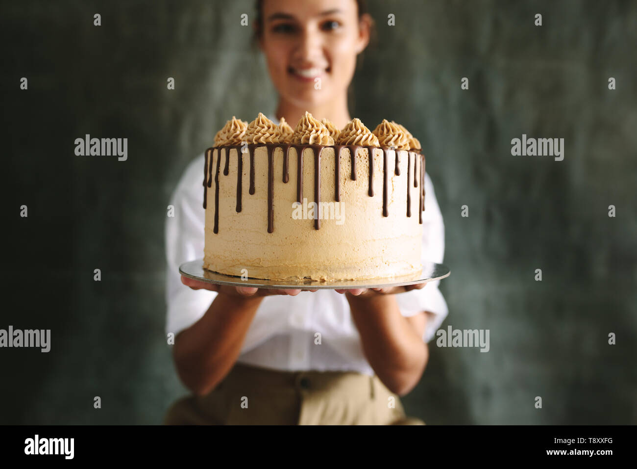 Baker Femmes tenant un délicieux gâteau. Chef holding gâteau fraîchement faite contre un arrière-plan gris. Banque D'Images