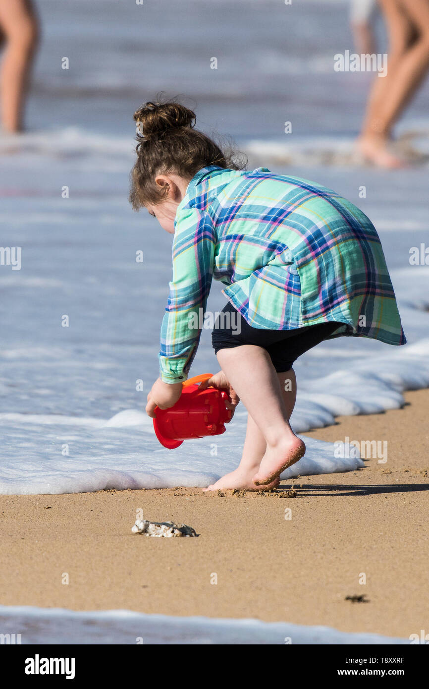 Un enfant en essayant de remplir son seau d'eau de mer sans se mouiller les pieds sur de Fistral Newquay en Cornouailles. Banque D'Images