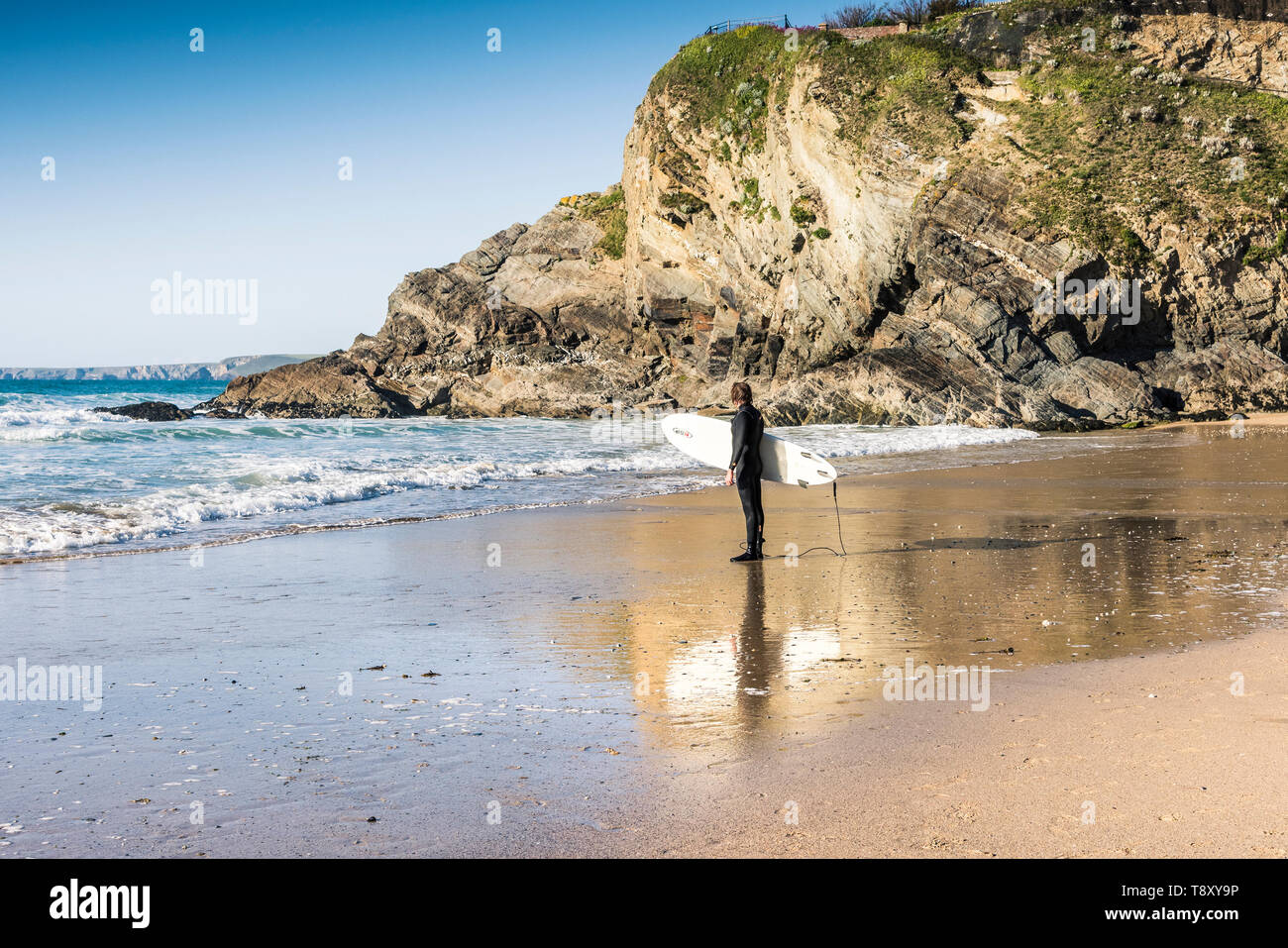 Un surfer carrying surfboard et son comité permanent sur la rive sur une grande plage de l'Ouest à Newquay en Cornouailles. Banque D'Images Un surfer carrying surfboard et son comité permanent sur la rive sur une grande plage de l'Ouest à Newquay en Cornouailles. Banque D'Images