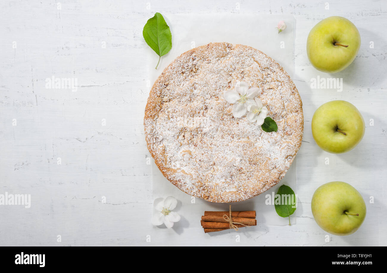 Mise à plat avec des délicieuses tartes aux pommes, pommes , fleurs de printemps , des feuilles et des bâtons de cannelle. Ronde maison tarte aux pommes sur le papier sulfurisé de sucre glace. Banque D'Images