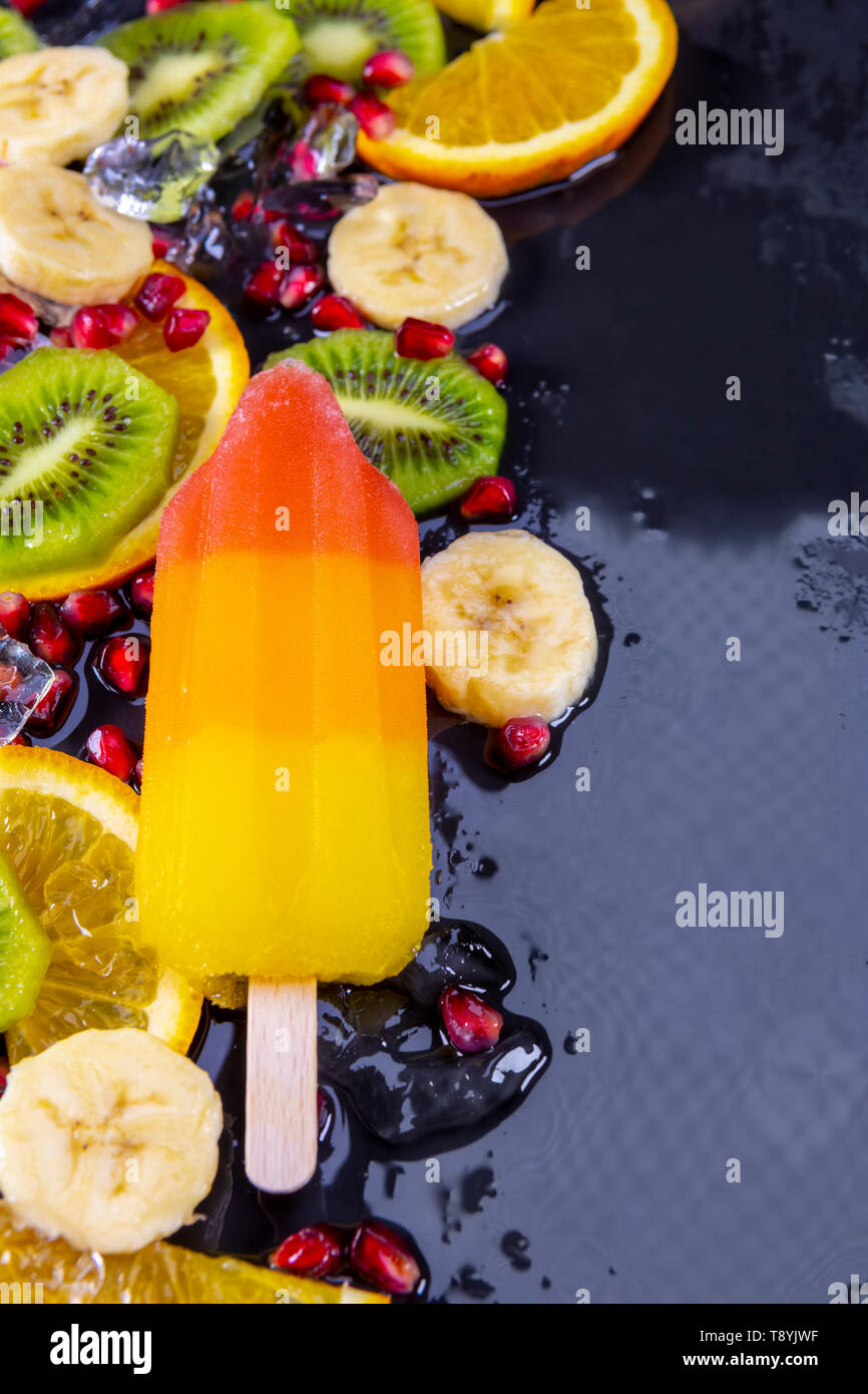 La crème glacée aux fruits sur stick avec des tranches de fruits sur l'ardoise noire. Se concentrer sur les sucettes glacées. Banque D'Images