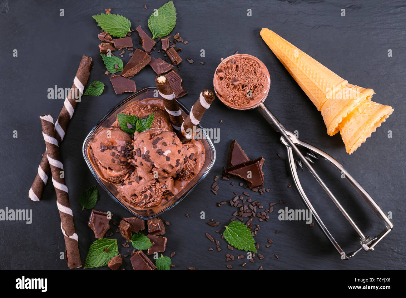 Boules de crème glacée au chocolat dans un bol en verre avec des bâtons, wafer cone et de chocolat sur une plaque en ardoise noire. Se concentrer sur la cuvette avec boules de crème glacée au chocolat Banque D'Images