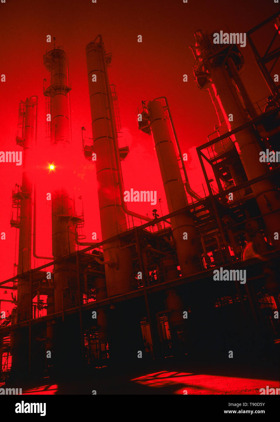 Une raffinerie de pétrole et le soleil vu à travers un filtre rouge Banque D'Images