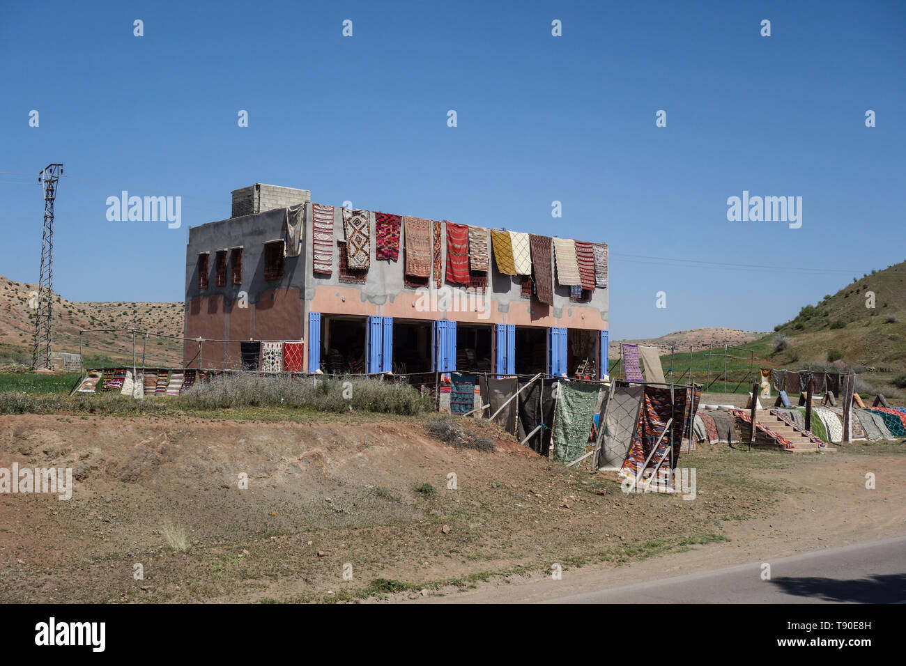 Des tapis colorés accrochés sur une chambre face à un village berbère dans l'Atlas de Marrakech, Maroc Banque D'Images