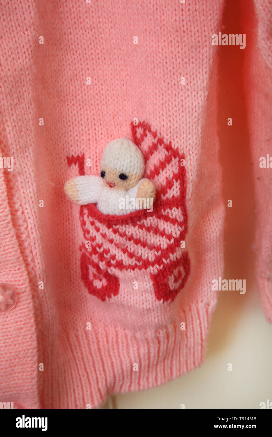 Une rose de l'enfant Cardigan en laine avec un bébé en buggy sur les poches Banque D'Images