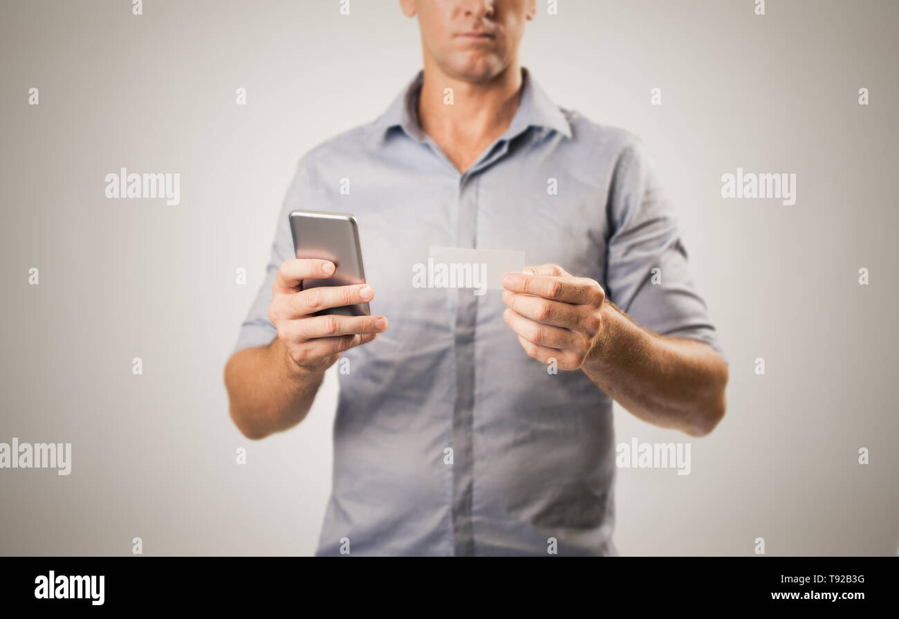 Young casual business man holding phone et carte de visite peut-être la prise de contact - concept d'affaires moderne de l'image sur fond blanc avec spa de copie Banque D'Images