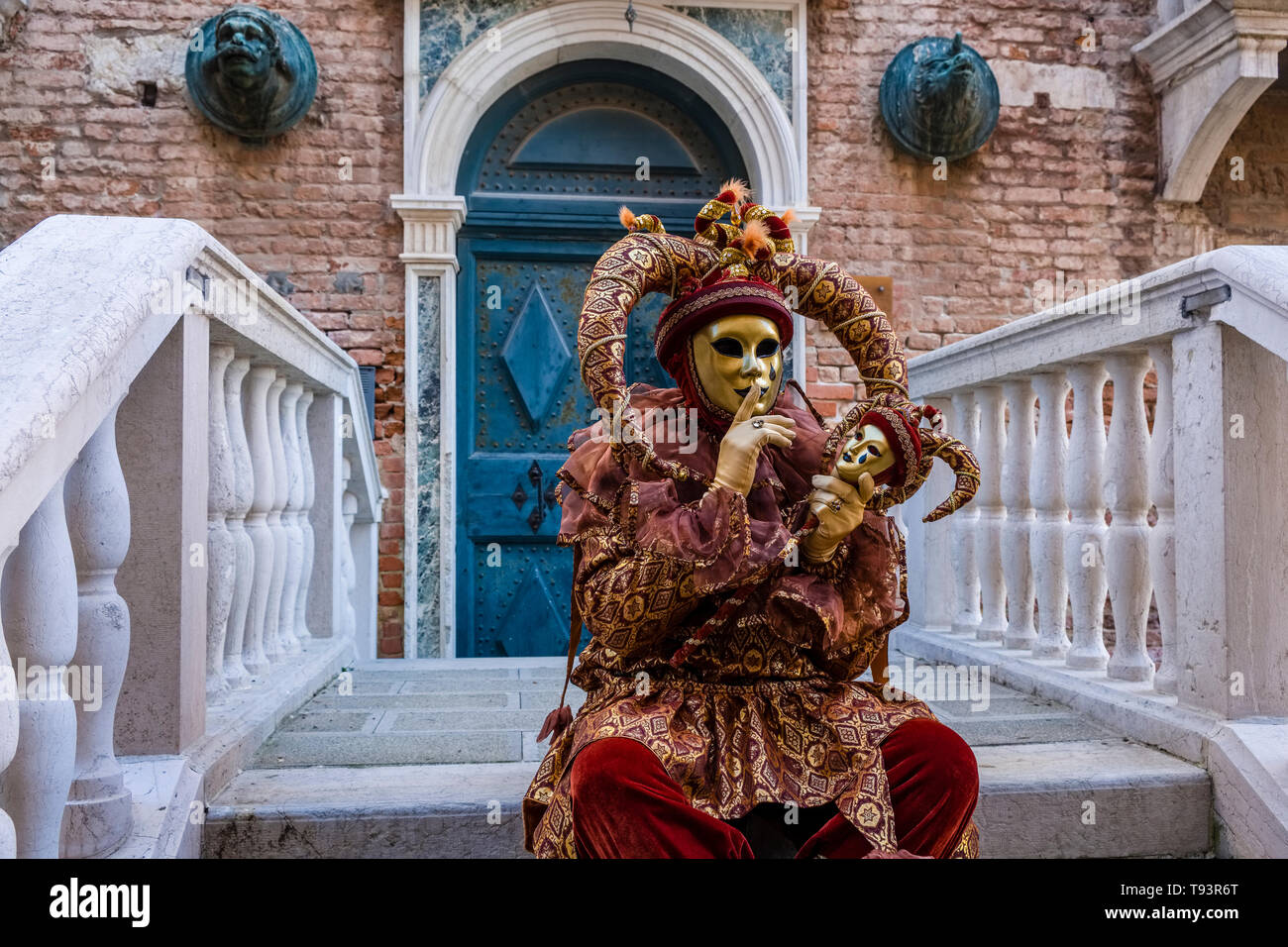 Portrait d'une personne masquée masculin dans un beau costume arlequin créative, posant sur un pont en face des bâtiments une porte, célébrant le Venet Banque D'Images