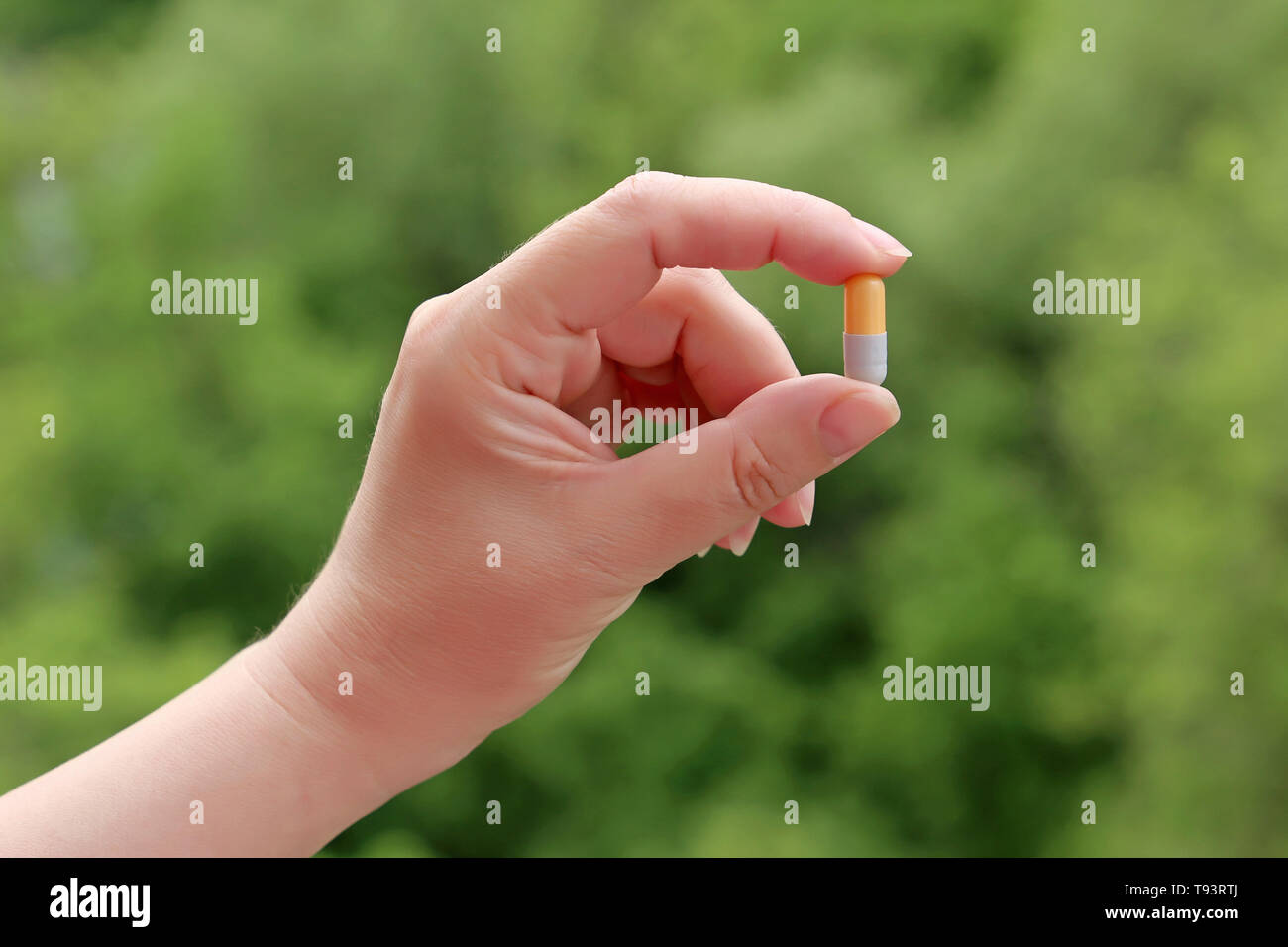 Comprimé dans la main féminine sur fond vert nature floue, girl holding médicament dans capsule close up. Concept de réputation, de traitement, de vitamines Banque D'Images
