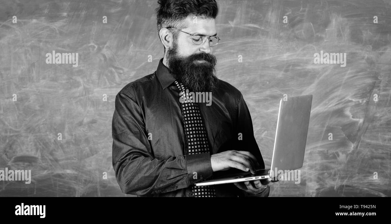 La technologie moderne de l'éducation. Professeur Hipster portent des lunettes et cravate est titulaire d'ordinateur portable. La technologie numérique de l'éducation. Commencer la leçon. Homme barbu enseignant avec ordinateur portable moderne tableau arrière-plan. Banque D'Images