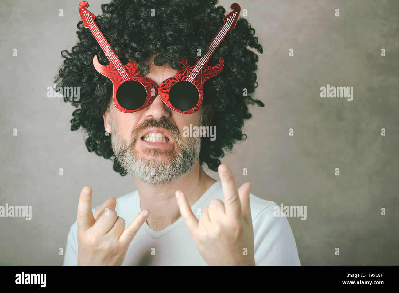Funny man with sunglasses faisant symbole rock avec les mains jusqu'à l'arrière-plan gris Banque D'Images