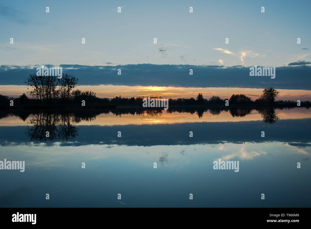 Un nuage sombre se reflétant dans le lac au coucher du soleil et d'arbres sur la rive Banque D'Images