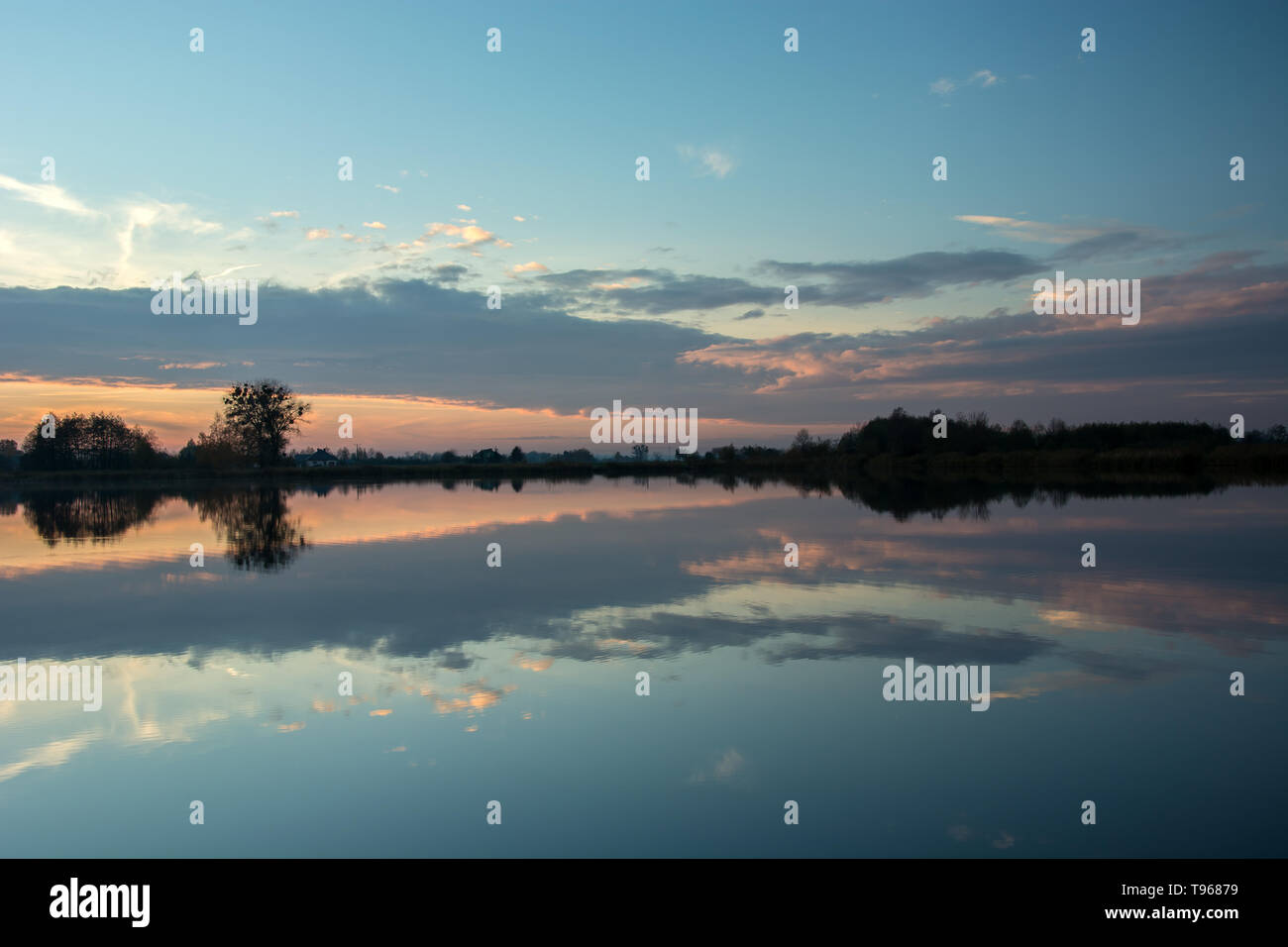 Soirée au bord du lac, les arbres sur la rive et la réflexion des nuages après le coucher du soleil dans l'eau Banque D'Images